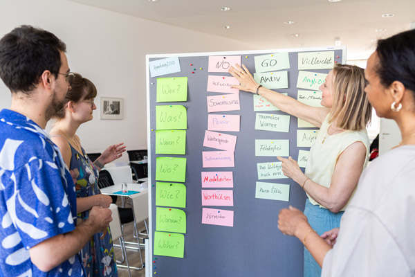Teilnehmer:innen und Dozentin stehen an einer Pinnwand.